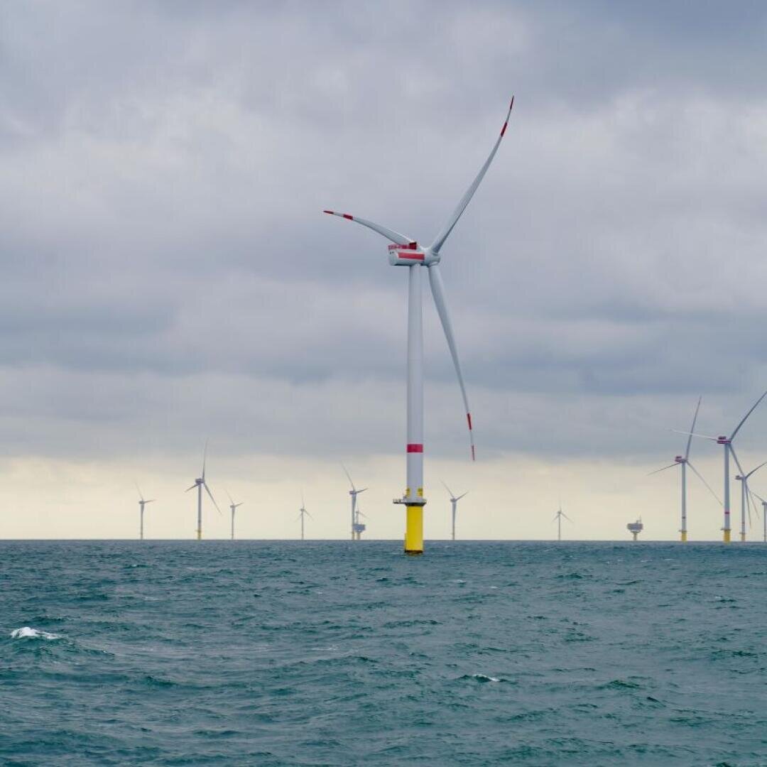 Offshore-Windkraftanlagen stehen unter einem bewölkten Himmel im Meer und erzeugen erneuerbare Energie. Das Wasser ist leicht unruhig, und man kann mehrere Windkraftanlagen erkennen, die sich in der Ferne verlieren.