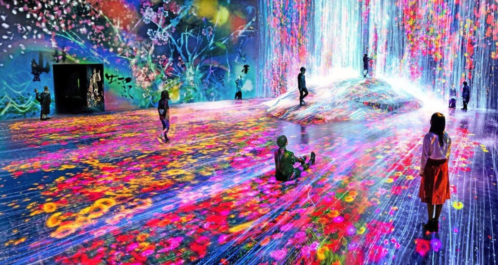 Children interact with a vibrant, immersive digital art installation featuring colorful flowing lights, virtual flowers, and animated projections on the walls and floor, creating a dynamic, dreamlike environment.