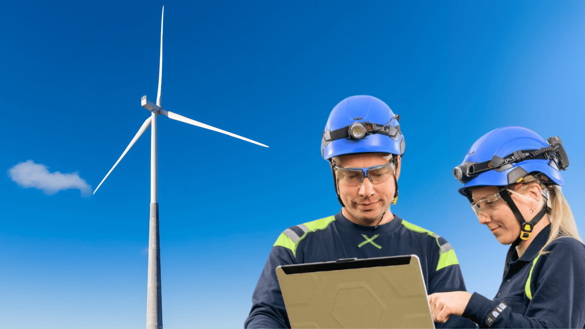 Zwei Arbeiter mit blauen Helmen und Sicherheitsausrüstung schauen im Freien auf einen Laptop, mit einer Windturbine und einem klaren blauen Himmel im Hintergrund, was auf den Betrieb oder die Wartung von Windenergieanlagen hindeutet.
