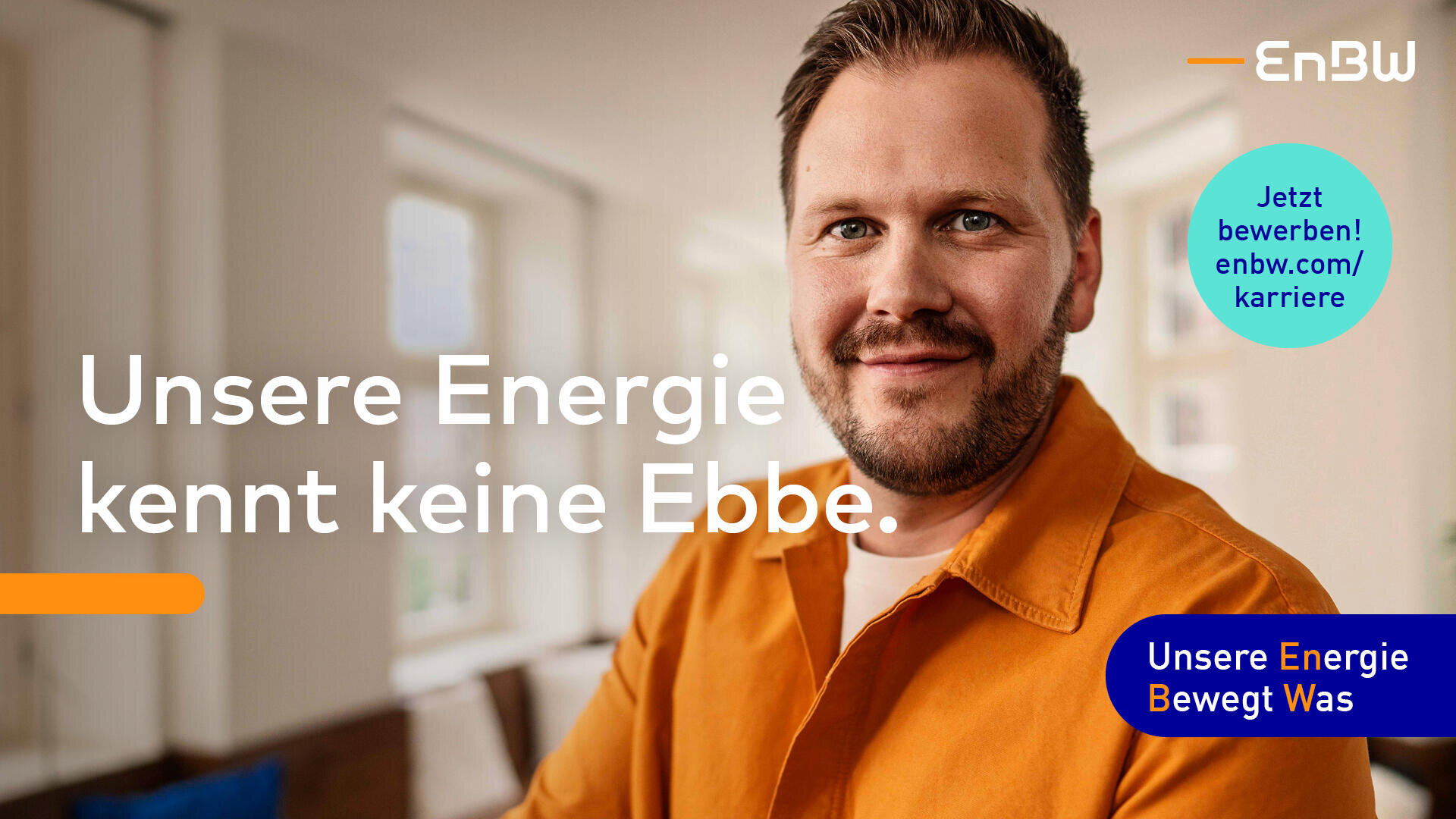 Ein lächelnder Mann in einem orangefarbenen Hemd sitzt in einem hellen Raum. Der deutsche Text lautet: Unsere Energie kennt keine Ebbe. Auf dem Bild erscheinen das EnBW-Logo und ein blauer Button mit Jetzt bewerben! enbw.com/karriere.