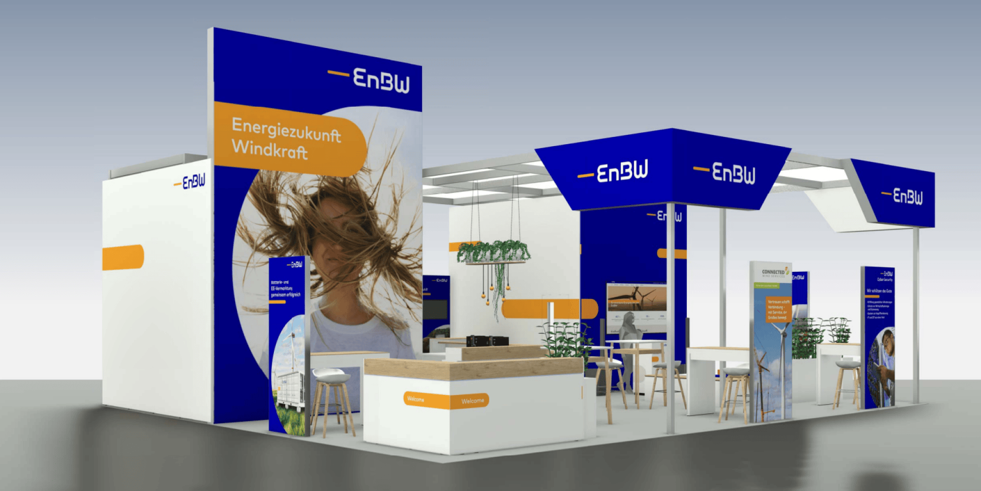 Ein moderner Messestand der EnBW mit blauen und weißen Paneelen, einem Schild mit der Aufschrift Energiezukunft Windkraft, einem großen Foto einer Frau mit windzerzausten Haaren, Stehtischen mit Hockern, Pflanzen und interaktiven Displays.