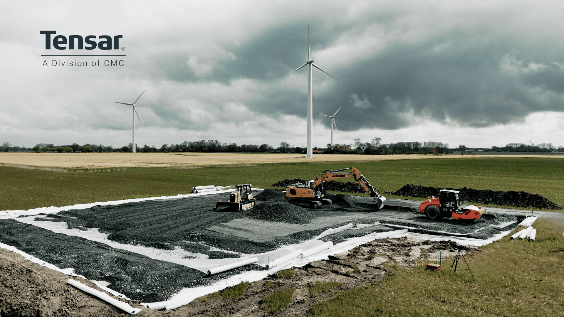 Baufahrzeuge bereiten ein Kiesfundament auf einem großen, offenen Feld mit Windturbinen im Hintergrund unter einem bewölkten Himmel vor. Das Tensar-Logo erscheint in der oberen linken Ecke.