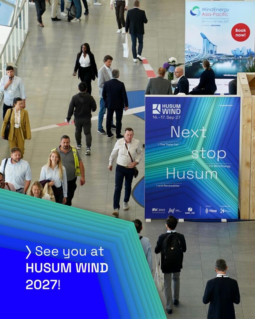 Menschen, die durch ein Kongresszentrum gehen und an einem großen, vertikalen Schild vorbeikommen, auf dem für die Messe Husum Wind im September 2027 geworben wird.