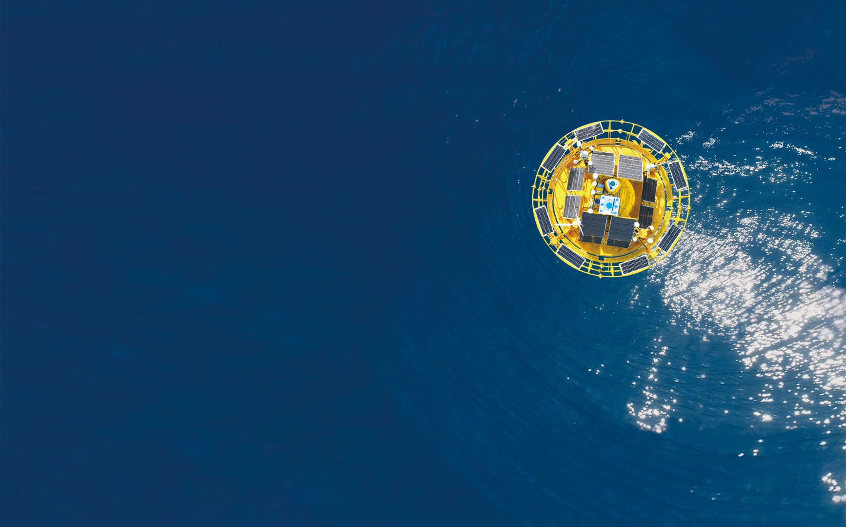 Luftaufnahme einer gelben Meeresboje mit Solarmodulen, die im tiefblauen Wasser schwimmt, sanfte Wellen erzeugt und das Sonnenlicht reflektiert.