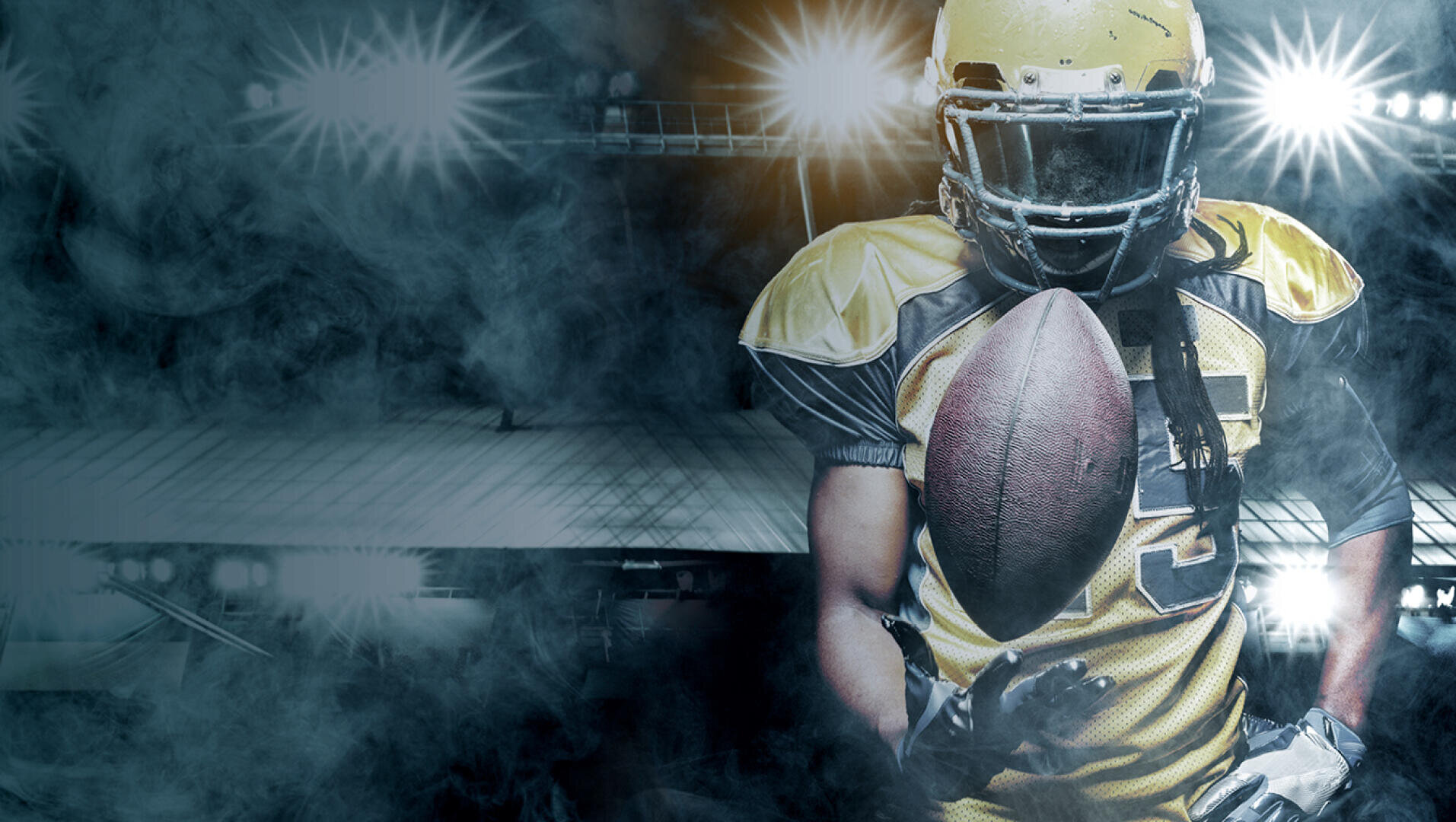 A football player in yellow gear and helmet stands on a smoky, illuminated field holding a football, while the stadium lights glow brightly in the background.