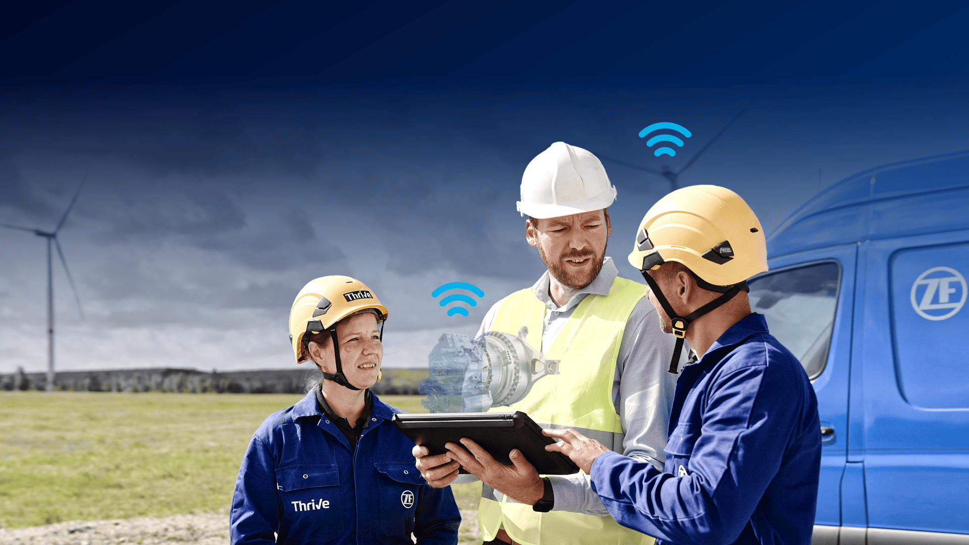Three workers in safety gear stand outdoors near a blue van with a wind turbine in the background. One holds a tablet displaying a digital engine model with wireless symbols above it, suggesting technology-driven collaboration.