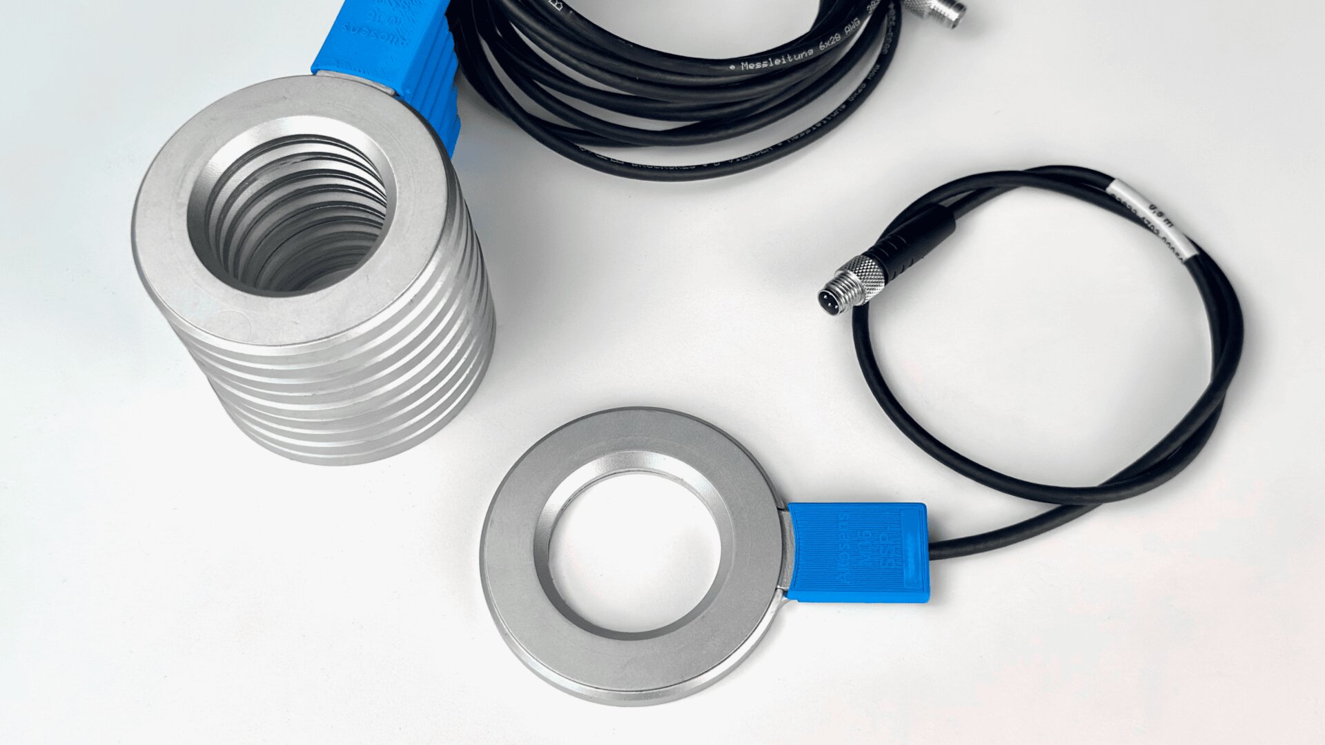Two metallic ring-shaped sensors with blue plastic sections are connected to black cables with connectors, placed on a white surface. One sensor is thicker with grooves, the other is slimmer and flat.
