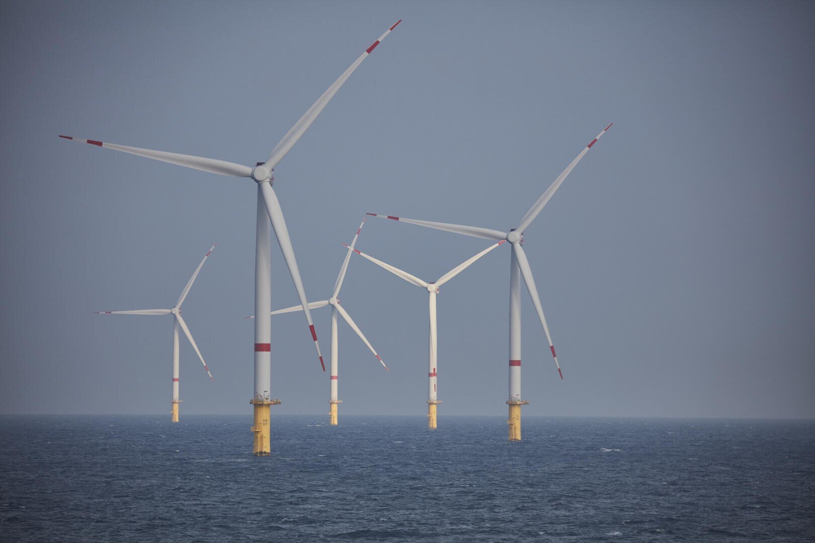 Mehrere große Offshore-Windturbinen stehen im Meer und erzeugen erneuerbare Energie. Der Himmel ist klar und das Wasser scheint unter den Turbinen ruhig zu sein.