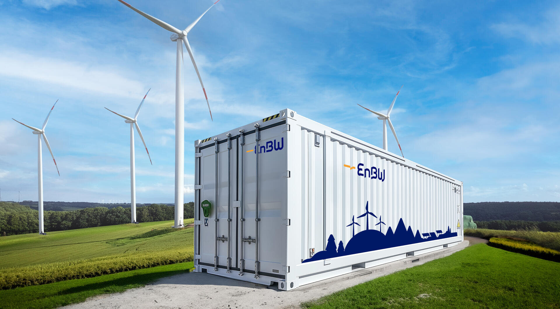 Ein großer weißer Container mit dem EnBW-Logo steht auf einem Feldweg in einer grünen Wiese, im Hintergrund drehen sich unter strahlend blauem Himmel mehrere Windräder.