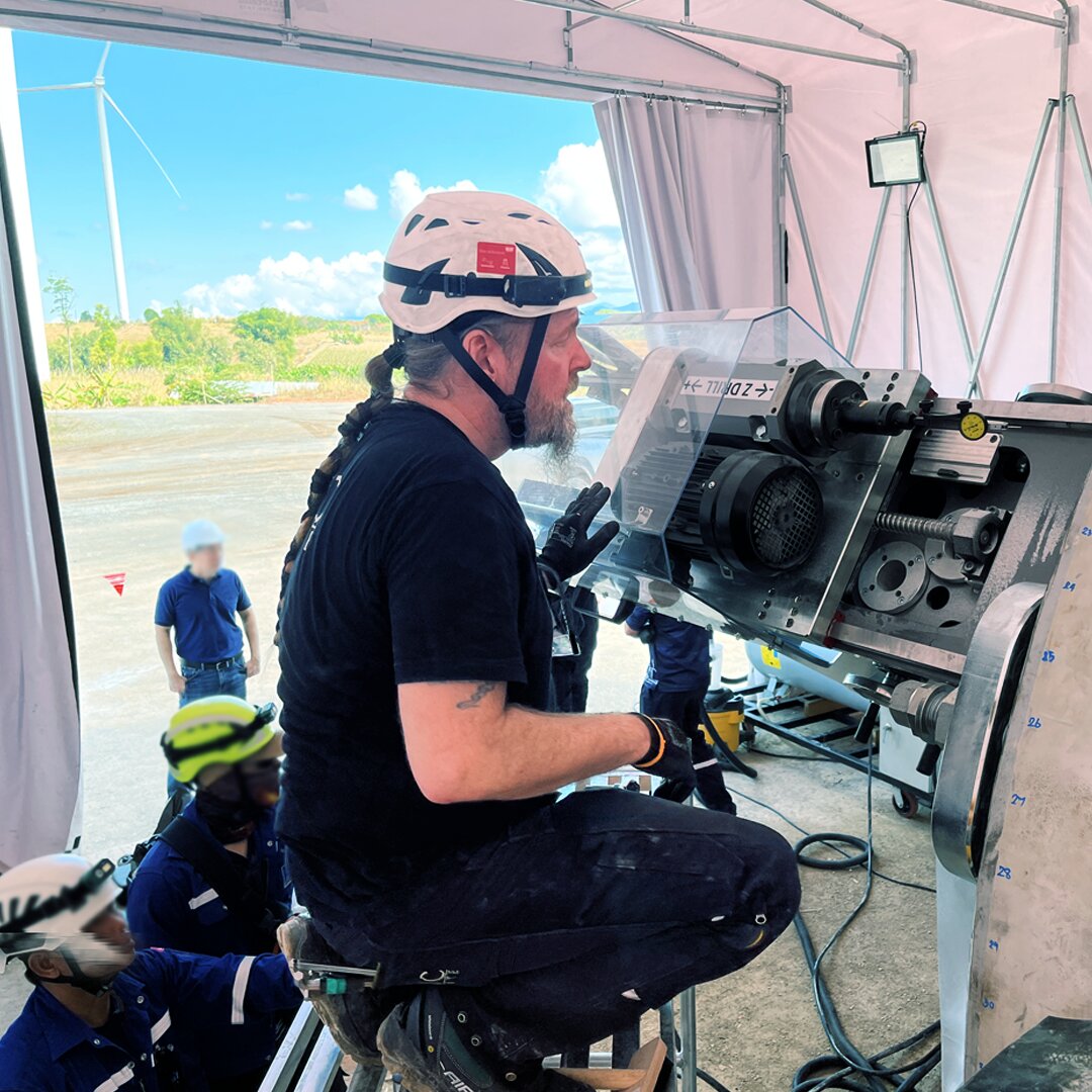 Ein Mann trägt einen Helm und sitzt auf einem Stuhl vor einer großen Maschine.