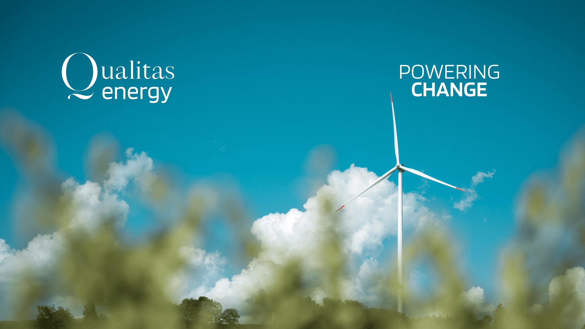 A wind turbine stands in front of a blue sky with scattered clouds. The words Qualitas energy and Powering Change appear in white lettering. Green foliage is blurred in the foreground.