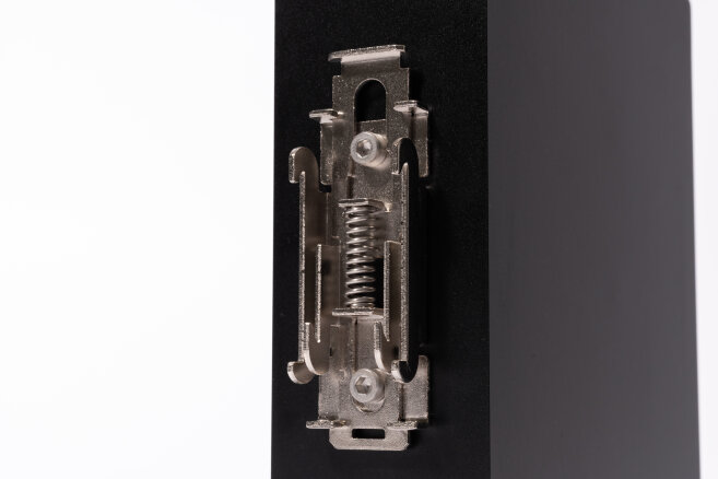Nahaufnahme eines Metallfederriegelmechanismus, der an der Kante eines schwarzen rechteckigen Objekts montiert ist, fotografiert vor einem weißen Hintergrund.