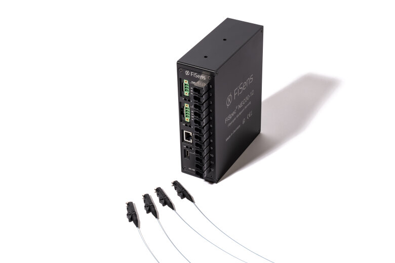 A black industrial network switch with multiple ports and indicator lights is standing upright. Four fiber optic cables with connectors are positioned in front of the switch on a white background.