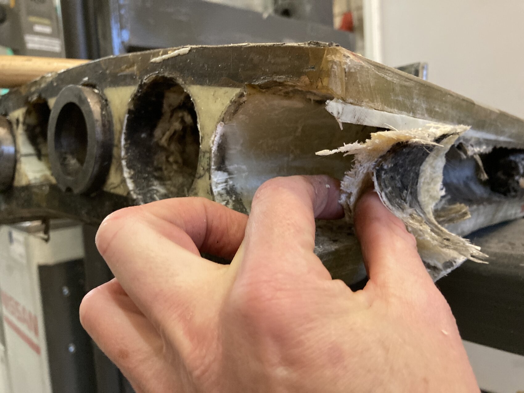 Nahaufnahme einer Person, die eine beschädigte Glasfaseroberfläche abzieht, wobei hohle zylindrische Abschnitte im Inneren des Materials zum Vorschein kommen.
